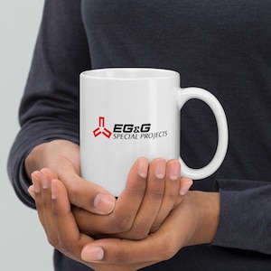 Puede incluir: Taza de cerámica blanca con un logotipo negro y rojo que dice "EG&G SPECIAL PROJECTS".
