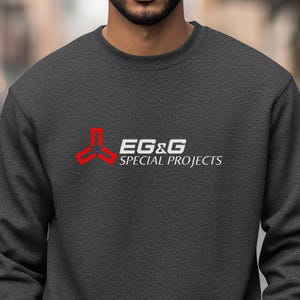 May include: A dark gray sweatshirt with a red and white logo. The logo is a stylized triangle with the text "EG&G SPECIAL PROJECTS" underneath.