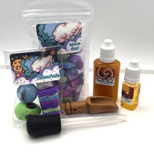 May include: A collection of colourful bath bombs, soaps, and liquids, packaged in clear bags and bottles. The bags are labelled "celestials" and "space dust." The bottles are labelled "Jupiter Storm" and "Scorching Flare."