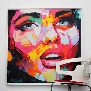 Könnte beinhalten: Abstrakte Malerei eines Frauen Gesichts mit leuchtenden Farben, darunter Pink, Gelb, Blau und Grün. Das Gemälde ist gerahmt und hängt an einer weißen Wand.