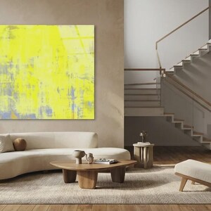 May include: A modern living room with a large abstract yellow painting. A curved beige sofa, wooden coffee table, and side tables complement the artwork. A wooden chair and staircase add to the contemporary design.