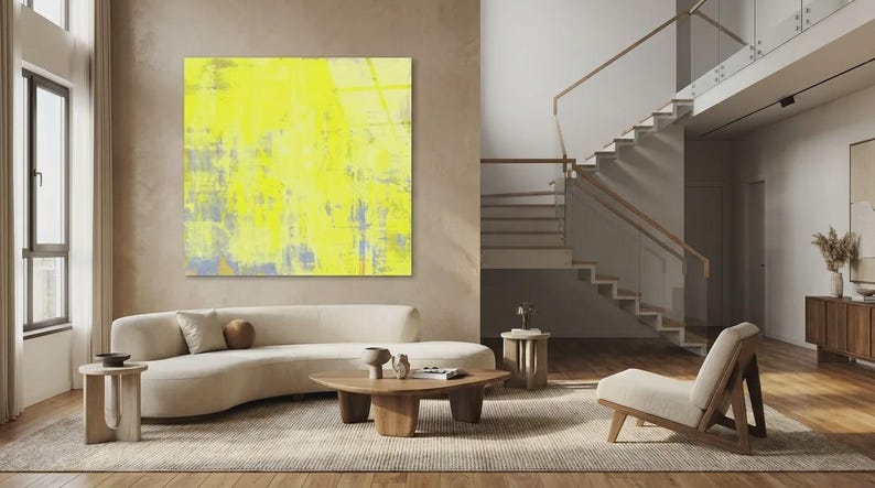 May include: A modern living room with a large abstract yellow painting. A curved beige sofa, wooden coffee table, and side tables complement the artwork. A wooden chair and staircase add to the contemporary design.