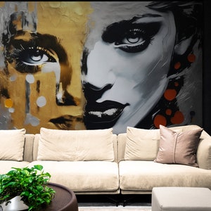 May include: A large abstract painting of a woman's face with a gold and silver background. The painting is hanging on a wall in a living room with a white sofa and a green plant in a pot on a coffee table.
