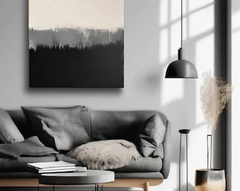 Puede incluir: Una pintura abstracta en blanco y negro con una línea horizontal que separa los dos colores. La pintura está colgada en una pared gris sobre un sofá gris con un cojín blanco. Una lámpara negra cuelga del techo sobre un jarrón dorado con flores secas.