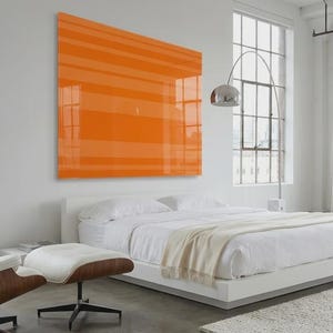 May include: A modern bedroom with a white bed, a brown and white lounge chair, and an orange artwork. The room has large windows and a neutral color palette, creating a bright and airy atmosphere. A chrome floor lamp adds a touch of elegance.