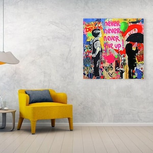 May include: A colorful graffiti art piece with the words "never give up" and silhouettes of people. The artwork is displayed on a wall above a yellow armchair and a small table. A modern lamp hangs from the ceiling.