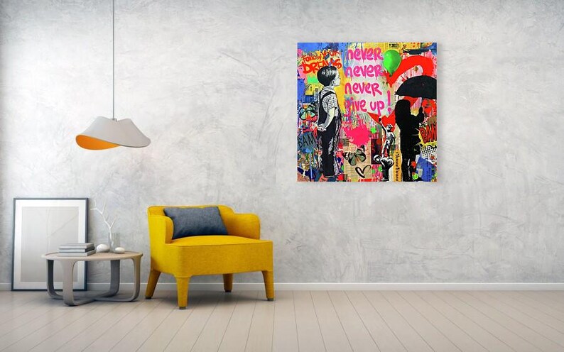 May include: A colorful graffiti art piece with the words "never give up" and silhouettes of people. The artwork is displayed on a wall above a yellow armchair and a small table. A modern lamp hangs from the ceiling.