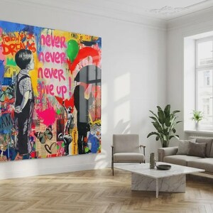 May include: A large, colorful artwork dominates a bright living room. The piece features graffiti-style art with the words "Follow Your Dreams" and "Never Give Up." A boy stands facing away, and a person holds a red umbrella.