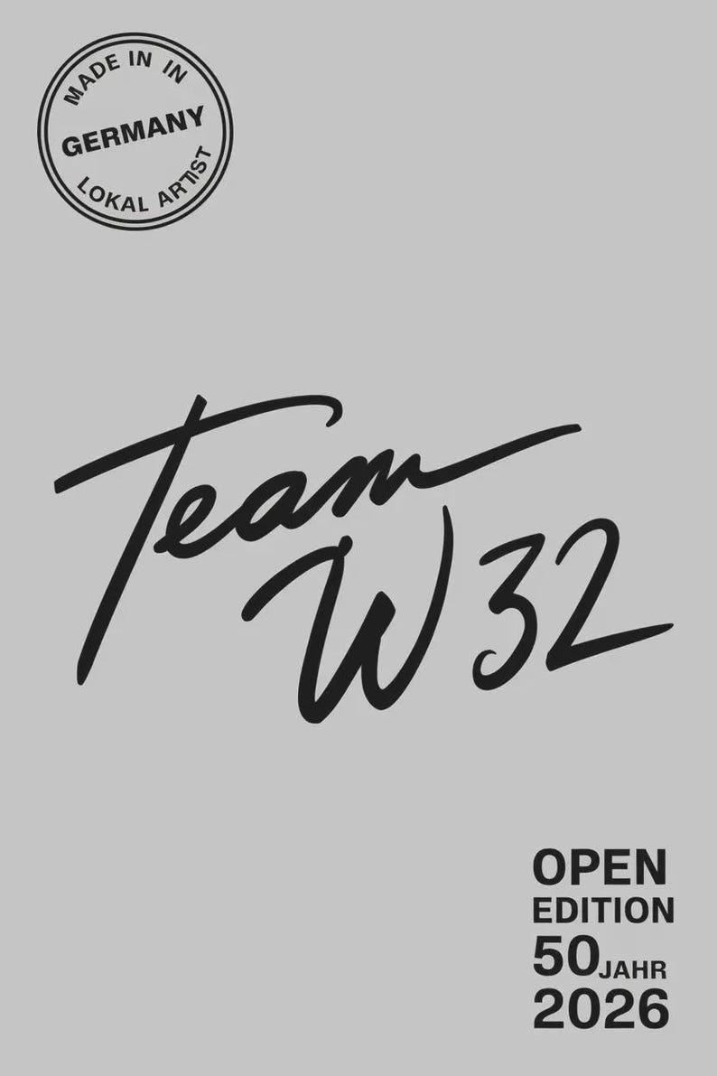 May include: A light gray background with the words "Team W32" in a black script font. Above the script is a circular stamp that reads "Made in Germany Lokal Artist". Below the script are the words "Open Edition 50 Jahr 2026".