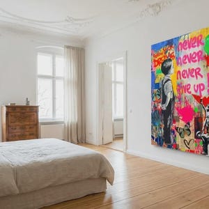 May include: A large, colorful Banksy-style artwork with the words "Never, Never, Never Give Up" dominates a bedroom wall. The artwork features silhouetted figures, graffiti-style elements, and vibrant colors, creating a bold statement piece.