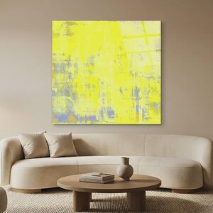 May include: A modern living room featuring a large abstract painting with yellow, blue, and gray brushstrokes. The room includes a beige sofa, two armchairs, a round wooden coffee table, and a floor lamp. The overall aesthetic is minimalist and contemporary.