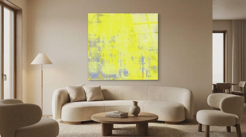 May include: A modern living room featuring a large abstract painting with yellow, blue, and gray brushstrokes. The room includes a beige sofa, two armchairs, a round wooden coffee table, and a floor lamp. The overall aesthetic is minimalist and contemporary.
