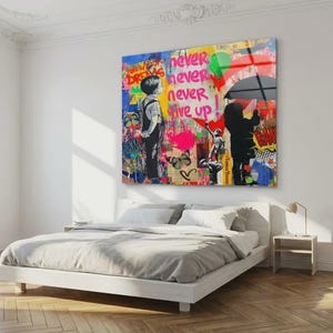 May include: A colorful pop art print with the words "never never never give up" in red and green. The artwork features two figures, one holding an umbrella, and is displayed above a white bed in a bright room.