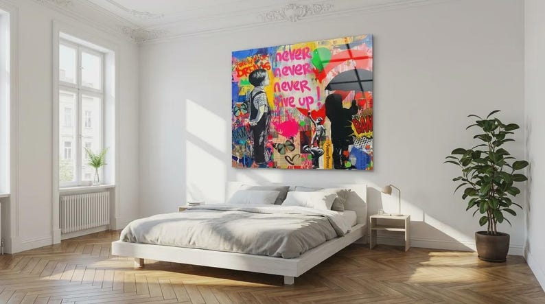 May include: A colorful pop art print with the words "never never never give up" in red and green. The artwork features two figures, one holding an umbrella, and is displayed above a white bed in a bright room.