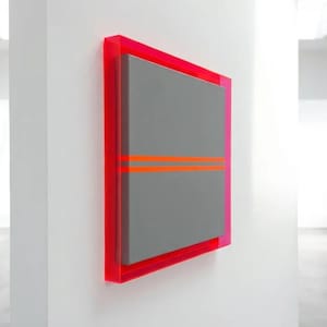 Op de afbeelding: Modern abstract kunstwerk. Een rechthoekig grijs paneel met twee horizontale oranje lijnen is ingekaderd in een felrode lijst. Het kunstwerk is aan een witte muur in een galerij bevestigd.