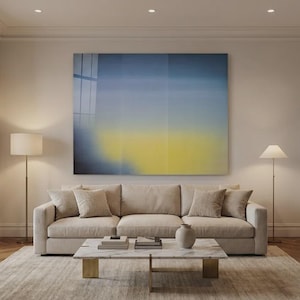 May include: A modern living room featuring a beige sofa, a marble coffee table, and two floor lamps. A large abstract painting with blue and yellow hues hangs above the sofa. The room has hardwood floors and a neutral color palette.