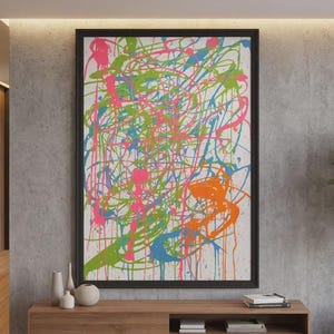 Könnte beinhalten: Abstrakter Kunstdruck in einem schwarzen Rahmen. Das Kunstwerk zeigt farbenfrohe Farbspritzer in Pink, Grün, Orange und Blau auf weißem Hintergrund. Das Gemälde wird über einem Holzschrank mit dekorativen Vasen und einer Pflanze ausgestellt.