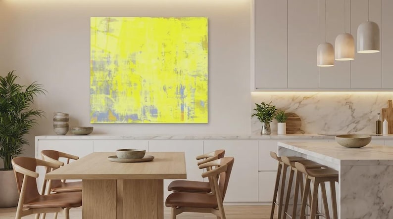May include: A modern kitchen with a large abstract yellow painting. The painting has a textured appearance with hints of gray and blue. The kitchen features a marble countertop, wooden chairs, and pendant lights.