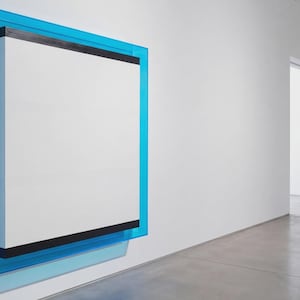 Puede incluir: Una obra de arte moderna montada en una pared blanca. La obra presenta un lienzo rectangular blanco enmarcado por un borde azul vibrante. Una franja negra acentúa la parte superior e inferior del lienzo. Se exhibe en una galería minimalista.