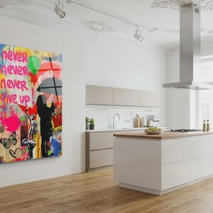 May include: A colorful Banksy-style artwork on a wall. The piece features a child looking at graffiti with the words "Never Never Give Up." The artwork is in a modern kitchen with white cabinets and a wooden floor.