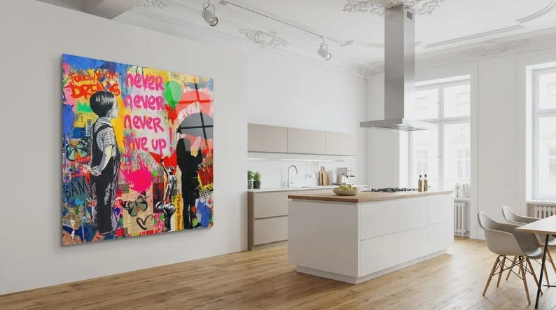 May include: A colorful Banksy-style artwork on a wall. The piece features a child looking at graffiti with the words "Never Never Give Up." The artwork is in a modern kitchen with white cabinets and a wooden floor.