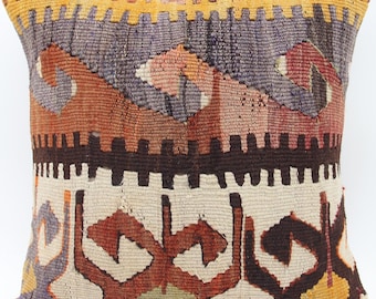 Puede incluir: Un cojín cuadrado con una funda de tejido textil con un patrón geométrico multicolor. El diseño incluye bandas horizontales de color amarillo, morado, naranja óxido, marrón oscuro y crema, mostrando intrincados motivos tribales.