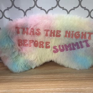 May include: A soft, pastel-coloured sleep mask with the text "TWAS THE NIGHT BEFORE SUMMIT" in pink and purple. The mask is a mix of pink, yellow, blue, and green, and has a soft, plush texture.