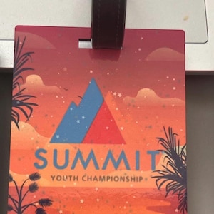 May include: Luggage tag with a sunset design, palm trees, and the text "SUMMIT YOUTH CHAMPIONSHIP" and "Tampa, FL *2025". The tag has a black strap for attachment.