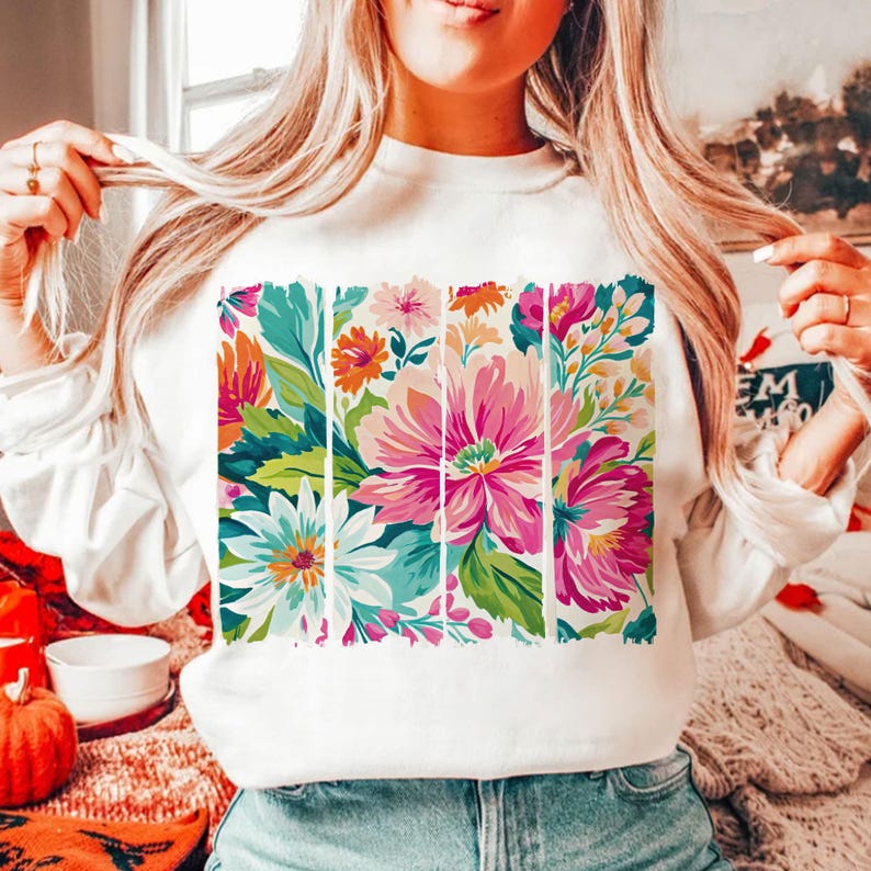 May include: White sweatshirt with a colorful floral print design. The print features a variety of flowers in shades of pink, blue, green, and yellow.