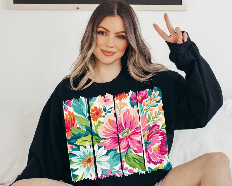 May include: Black sweatshirt with a colorful floral print design. The print features a variety of flowers in shades of pink, orange, yellow, green, and blue. The flowers are arranged in a vertical pattern and are surrounded by a white background.