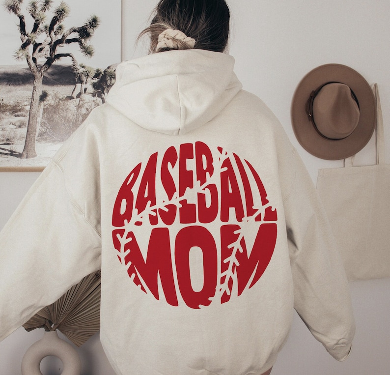 May include: A cream-colored hoodie with a red baseball graphic that says "Baseball Mom" on the back.