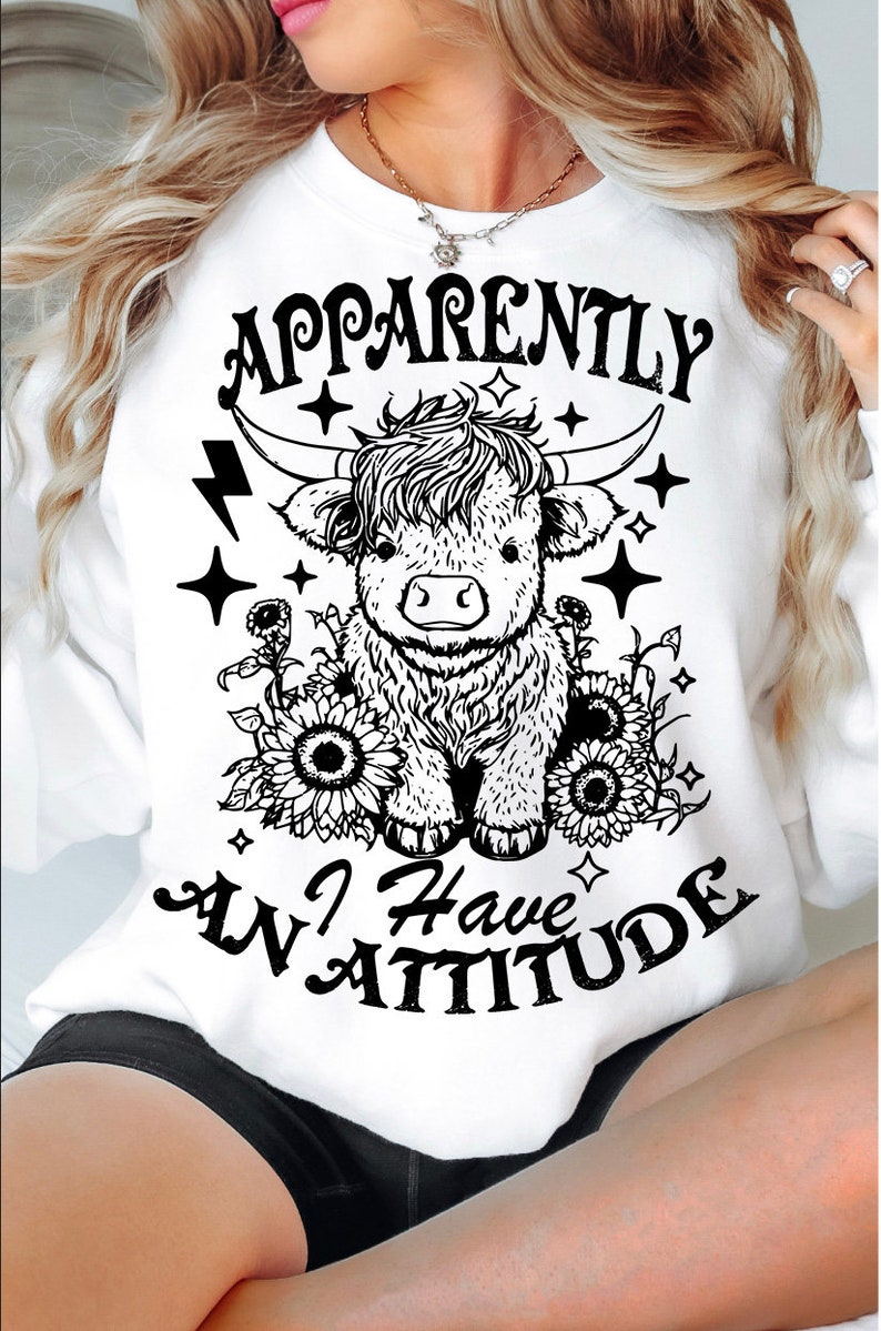 May include: White sweatshirt with a black and white illustration of a Highland cow with the text "Apparently I Have An Attitude" printed on it.