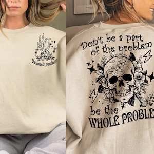 May include: A beige sweatshirt with a black skull and floral design on the back. The text "Don't be a part of the problem be the WHOLE PROBLEM" is printed on the sweatshirt. The front of the sweatshirt has a black skeleton hand with the text "the whole problem" printed on it.