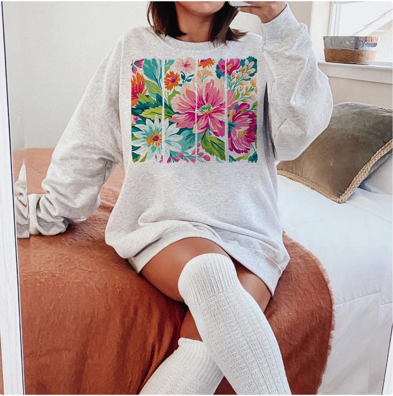 May include: A gray sweatshirt with a floral print design. The print features a variety of flowers in shades of pink, white, and green.