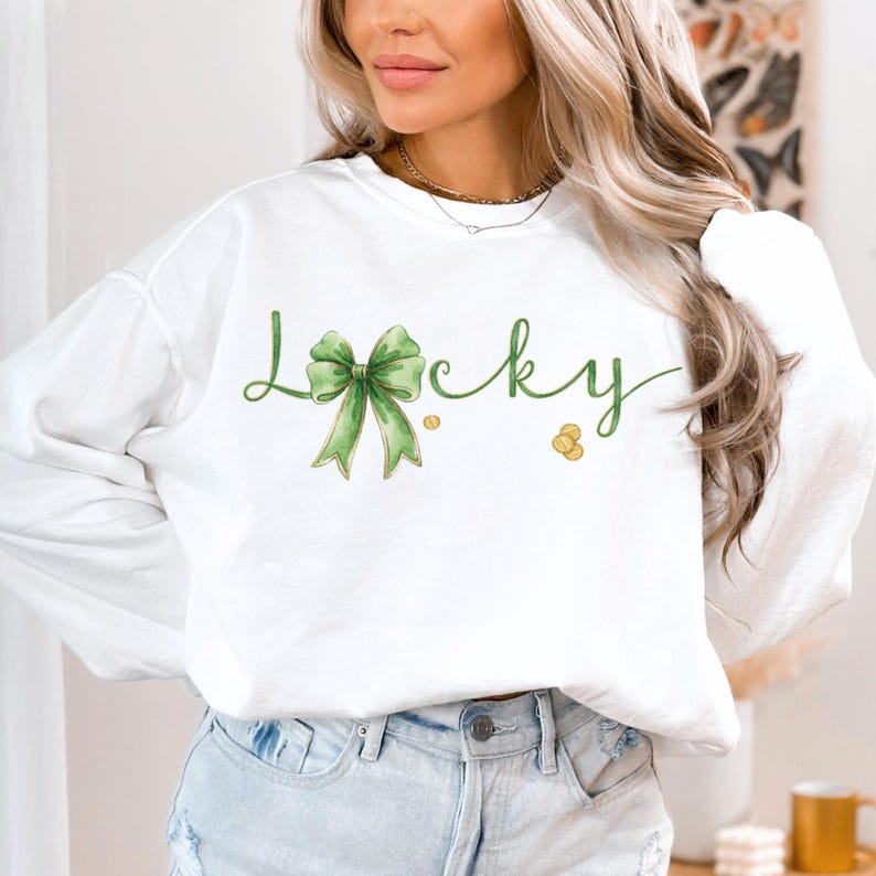 May include: White sweatshirt with the word "Lucky" in green script, featuring a green bow and gold coins. The long-sleeved top is a casual style, perfect for St. Patrick's Day or everyday wear.