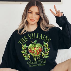 以下が含まれることがあります： 緑のリンゴのグラフィックと「The Villains Social Club Villains Do It Better」というテキストが書かれた黒いスウェットシャツ。