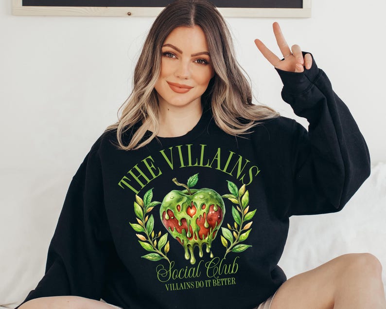 以下が含まれることがあります： 緑のリンゴのグラフィックと「The Villains Social Club Villains Do It Better」というテキストが書かれた黒いスウェットシャツ。