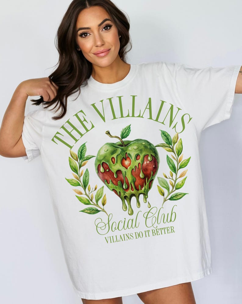 以下が含まれることがあります： 緑のリンゴのグラフィックと「The Villains Social Club」と「Villains Do It Better」のテキストが書かれた白いTシャツ。