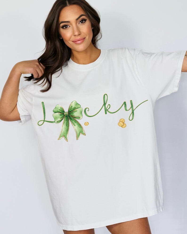 May include: White t-shirt with the word "Lucky" in green script, featuring a green bow and gold coins. The shirt is a loose fit, suitable for casual wear. The design has a watercolor effect, perfect for St. Patrick's Day.