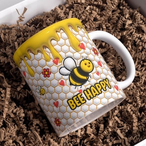 May include: A white ceramic mug with a yellow dripping honey design. The mug has a honeycomb pattern with a cartoon bee and the text "Bee Happy".