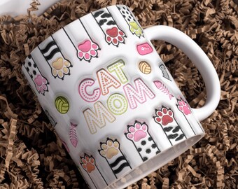 May include: White ceramic mug with a colorful paw print and cat-themed design. The mug says "CAT MOM" in pink, green, and yellow letters with white polka dots.