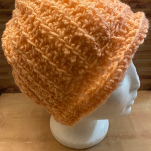 Peut inclure: Un bonnet en crochet de couleur pêche sur une tête de mannequin blanche.