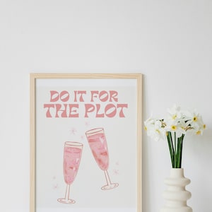May include: A framed print with the text "Do it for the plot" in pink lettering. Two pink champagne glasses clink together with sparkling stars around them.