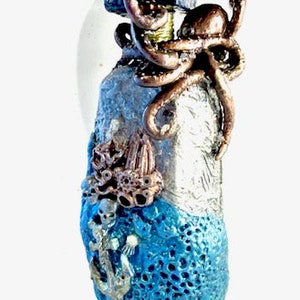 May include: A blue and silver ceramic table with an octopus design. The table top is round and has a textured surface. The base of the table is shaped like a bottle and has a blue and silver design with an anchor and coral.