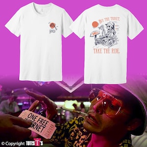 Puede incluir: Dos camisetas blancas. Una tiene un pequeño diseño naranja y azul con la palabra "GONZO". La otra presenta un esqueleto conduciendo un coche con el texto "BUY THE TICKET, TAKE THE RIDE." Ropa casual.