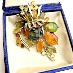 May include: A floral-shaped brooch featuring silver-tone metal stems and leaves accented with multi-colored, translucent, teardrop-shaped cabochons in shades of olive green, amber, and yellow, along with small, round, sparkling orange and yellow rhinestones.
