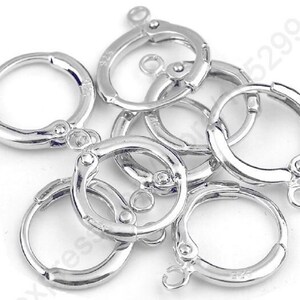 May include: A close-up of six silver-toned earring hoops with a hinged clasp. The hoops are arranged in a pile, with some overlapping.