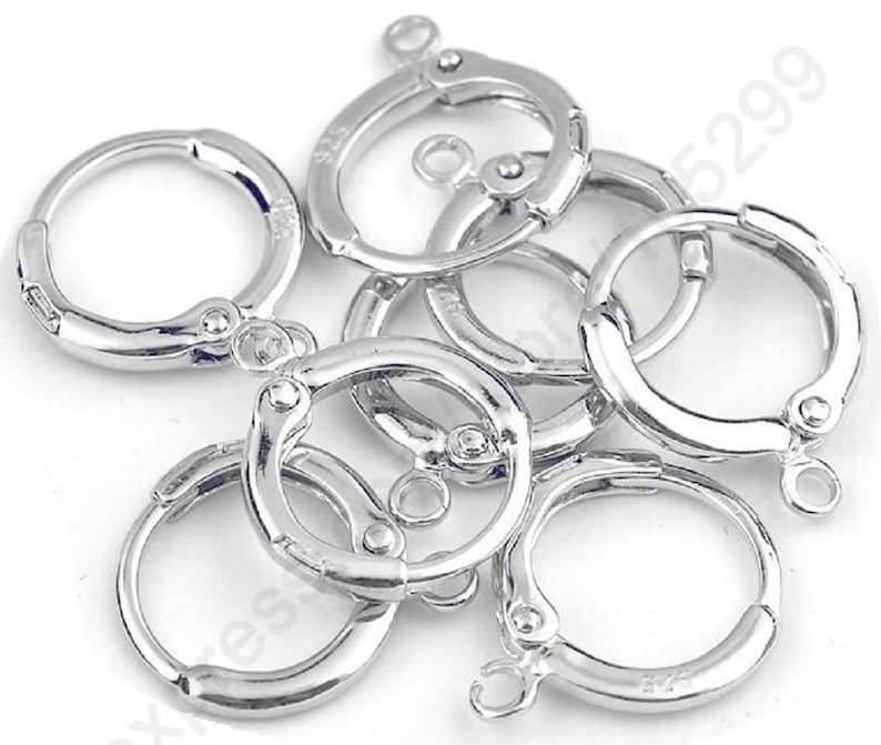 May include: A close-up of six silver-toned earring hoops with a hinged clasp. The hoops are arranged in a pile, with some overlapping.