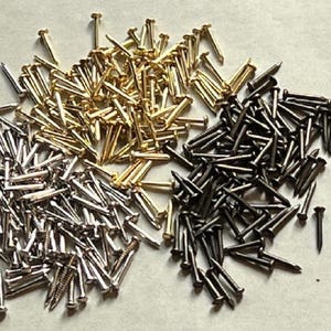 May include: A large pile of mixed metal tacks. The tacks are silver, gold, and black.