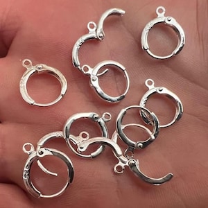 May include: A close-up of a group of silver earring hoops with a clasp closure. The hoops are arranged in a random pattern on a hand.